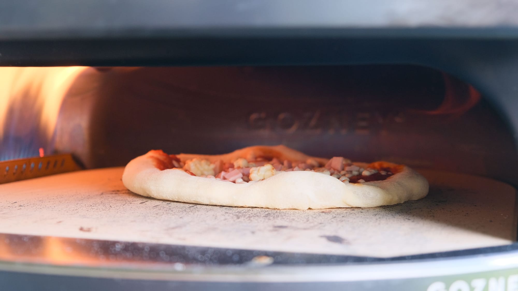 A partially baked pizza cooking on the stone floor inside the Gozney Arc XL home pizza oven.