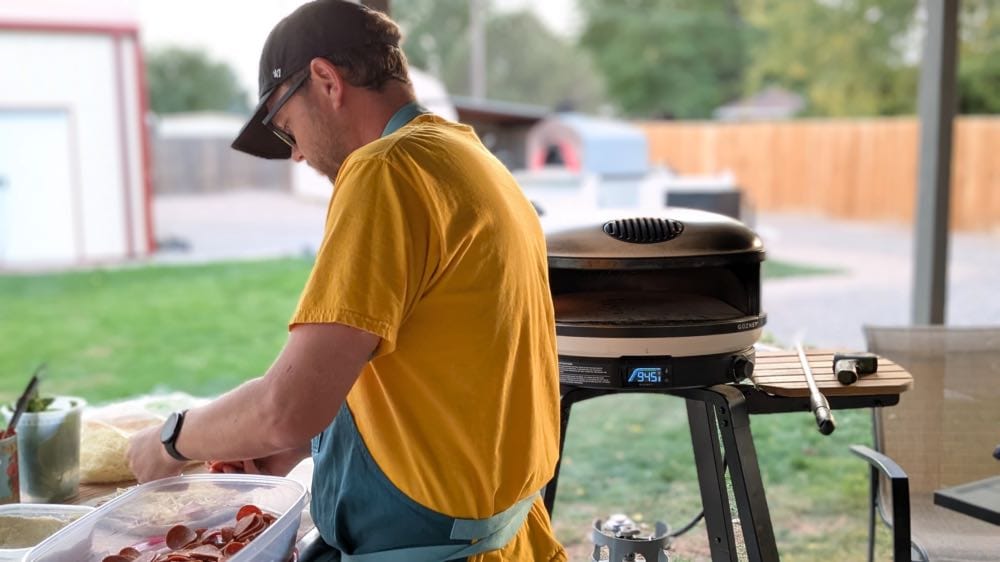 Jason preparing a pizza on an outdoor prep table next to a hot Gozney Arc XL pizza oven on its stand.
