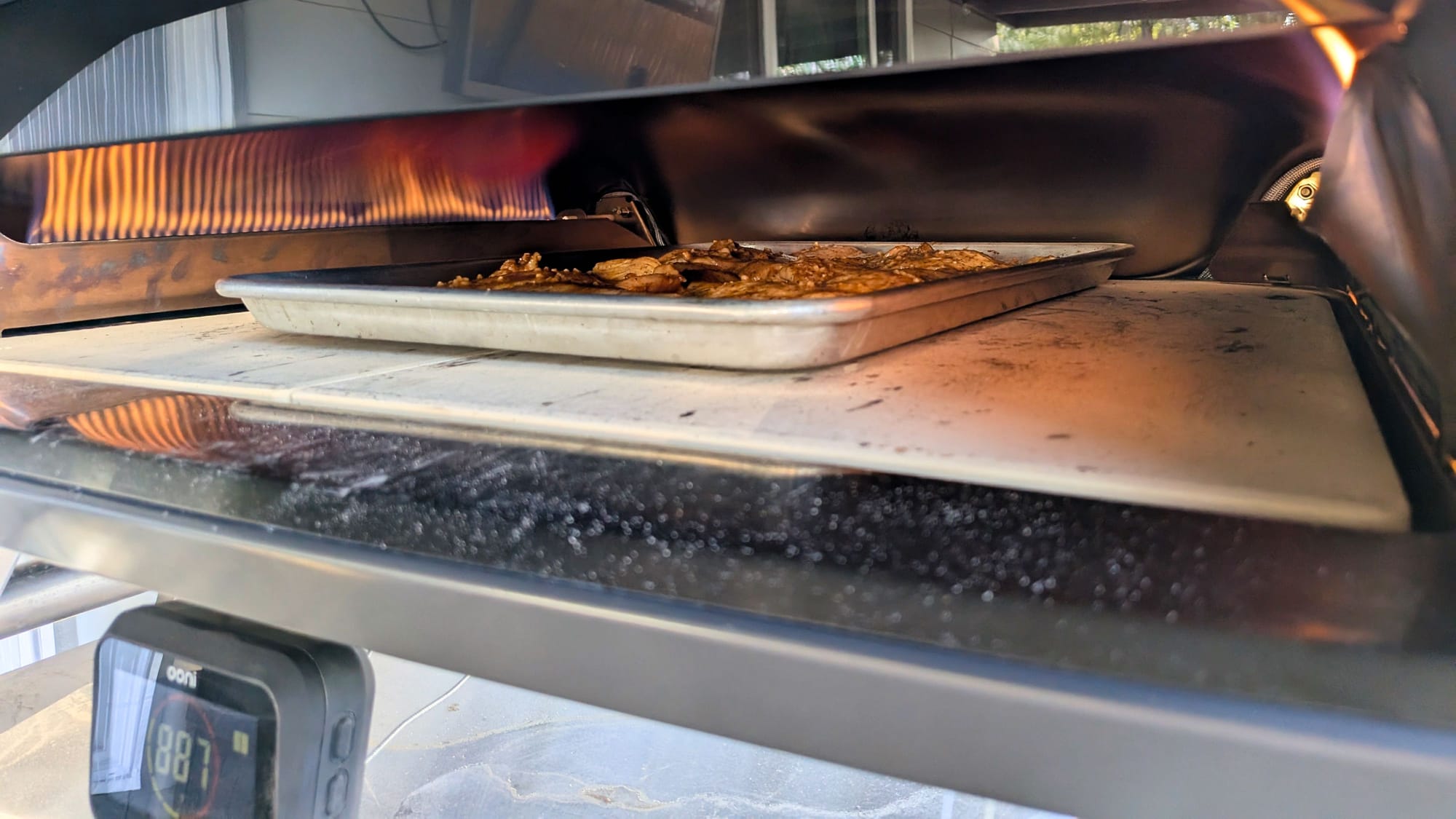 A metal baking sheet filled with food roasting inside the Ooni Koda 2 Max under a rolling, continuous gas flame.