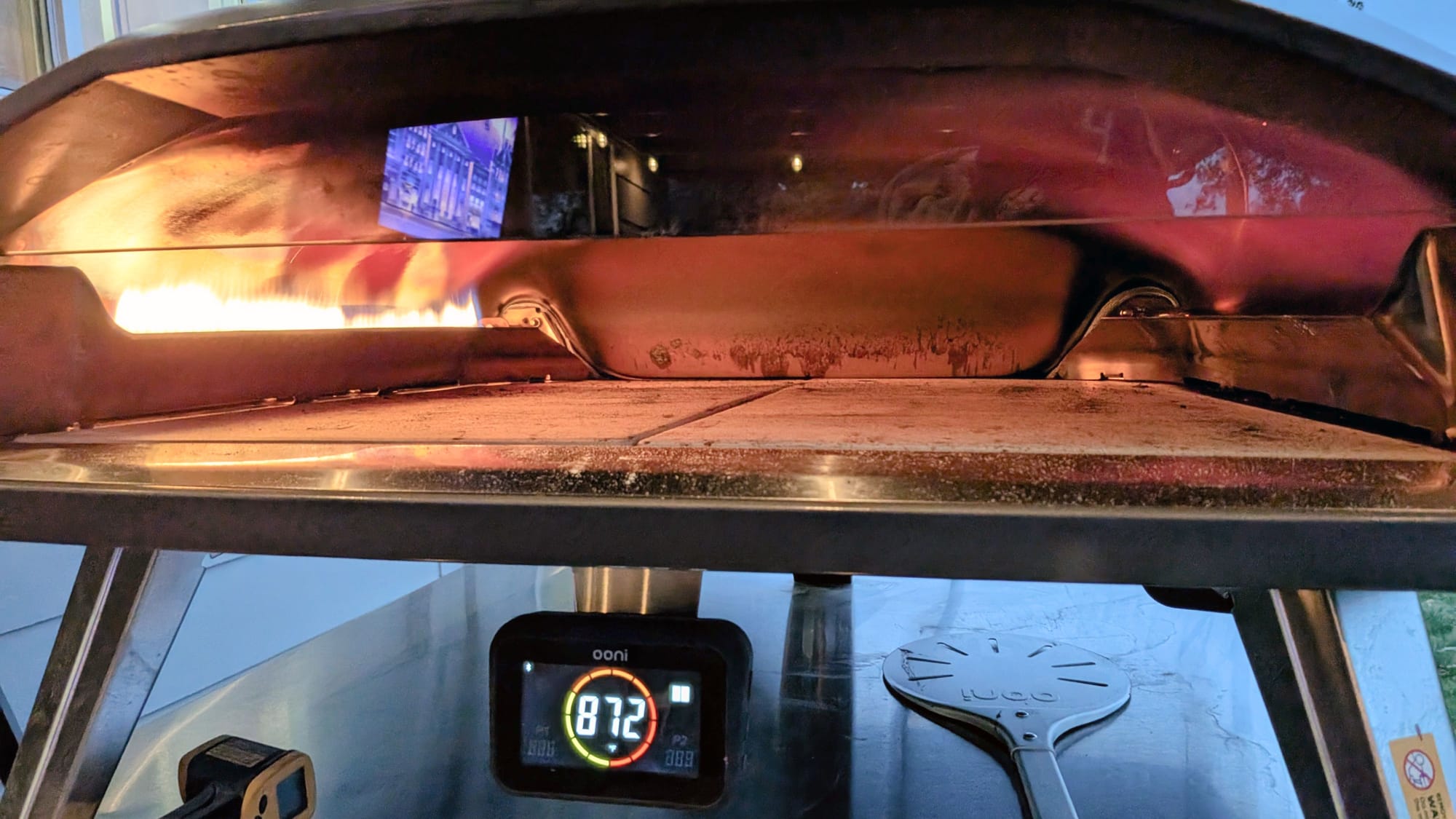 The interior of the empty Ooni Koda 2 Max pizza oven showing the dual gas burners and a digital temperature display reading 872 degrees Fahrenheit.