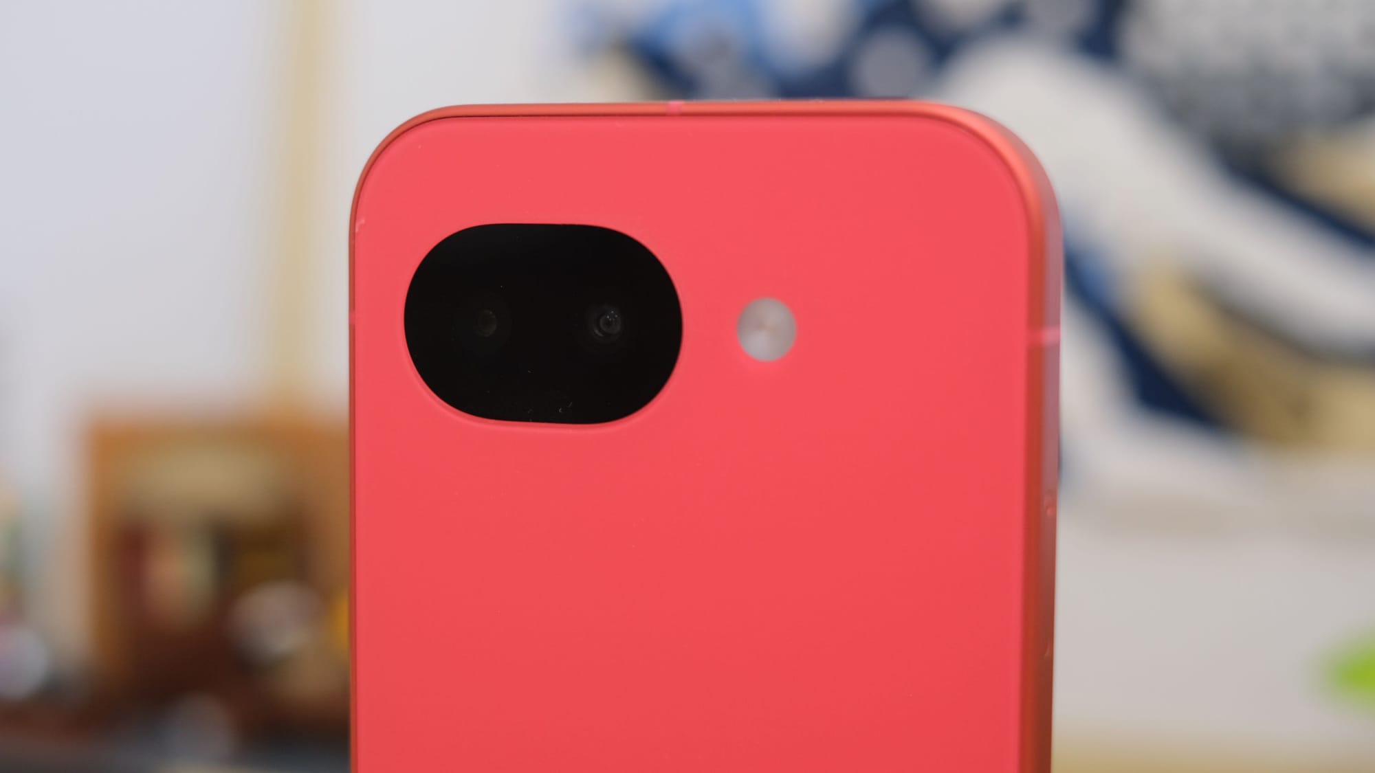 A close-up shot focusing on the upper back of the coral phone, highlighting the glossy black dual-camera module and the circular flash against the matte pinkish-orange body.